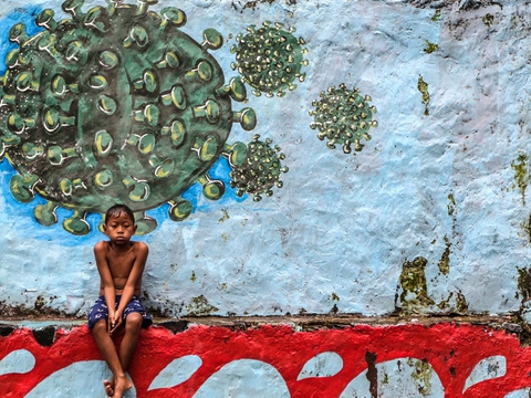 En dreng sidder under et murmaleri af coronavirusset i Vestjava i Indonesien. Landet har bekræftet over 278.000 tilfælde af coronasmitte og har ifølge de officielle tal lidt over 10.400 dødsfald blandt smittede.