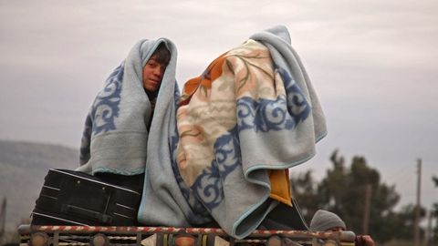 Syriske børn har pakket sig ind i tæpper, mens de den 11. februar 2020 sidder bag på en lastbil nær byen al-Ghazawiya og flygter fra angreb på landbrugsområder vest for Aleppo.