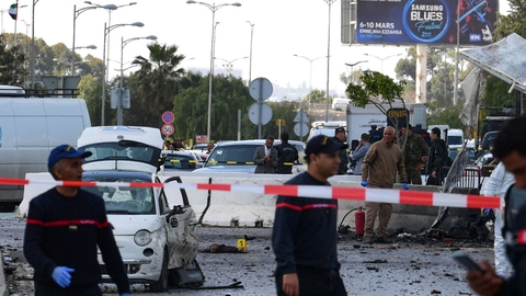 I forgrunden er kriminalteknikere på arbejde, efter to personer på en motorcykel har detoneret en sprængladning ved USA's ambassade i Tunis.