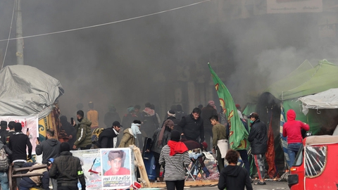 Irakiske demonstranter går rundt blandt brændende telte på Tahrir-pladsen i Bagdad, som sikkerhedsstyrker forsøgte at rydde lørdag.